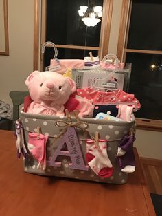 a pink teddy bear sitting in a baby's diaper basket on top of a wooden table