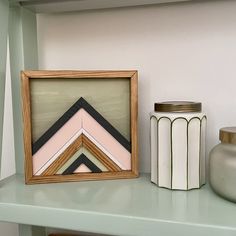 a wooden frame sitting on top of a shelf next to a vase and container filled with flowers