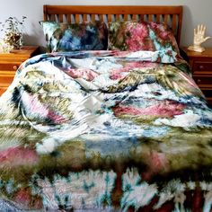 a bed with a colorful comforter and pillows on top of it, next to a night stand