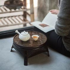 a person sitting down reading a book and drinking tea