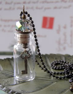 a glass bottle with a key inside sitting on a table next to a beaded necklace