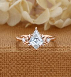 a white diamond ring sitting on top of a wooden table next to flowers and petals