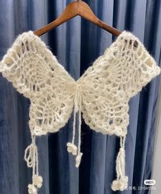 a white crocheted shawl hanging on a wooden hanger in front of a blue curtain