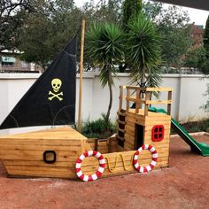 a wooden pirate ship playground set up in a yard with a pirate flag on it