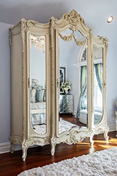 an ornately decorated white armoire with mirrors on the doors and drawers, in front of a large mirror