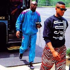 two men are walking down the street in front of a bus and another man is wearing sunglasses