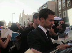 a man in a suit signing autographs for fans at an event with other people