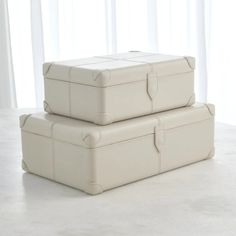 two white leather suitcases sitting on top of each other in front of a window