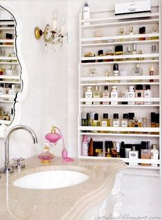 a bathroom sink sitting under a mirror next to a shelf filled with bottles and cosmetics