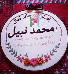 a white embroidered sign with flowers and words in arabic writing on the bottom, along with a black bow