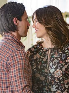 a man and woman standing next to each other in front of a wall with flowers on it