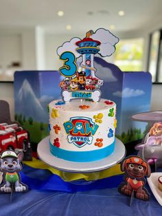 a birthday cake with paw patrol characters on it sitting on a table next to other toys