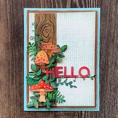 a card made with the word hello and mushrooms on top of green leaves, wood background