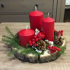 three red candles sitting on top of a wooden table next to pine cones and berries