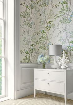 a white dresser sitting in front of a window next to a wallpapered wall