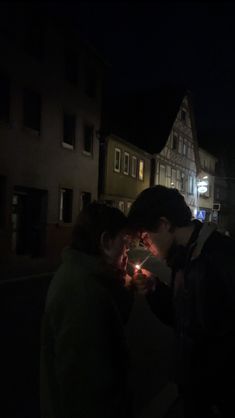 two people standing in front of a building at night with a lit candle on the ground