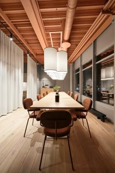 a large wooden table surrounded by brown chairs and white drapes in a room with wood flooring