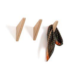 two pieces of wood hang from hooks on a white wall, one with an orange and black polka dot scarf