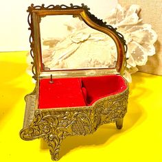 an ornate wooden box with a red cushion in it on a yellow surface next to a white flower