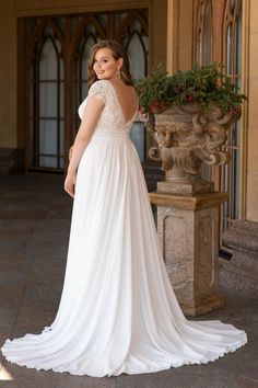 a woman standing in front of a building wearing a white wedding dress with an open back