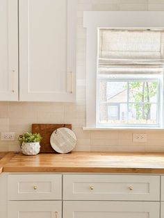 a kitchen with white cabinets and wooden counter tops next to a window that has a potted plant on it