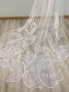 a white veil with flowers on it sitting on top of a wooden floor next to a wall