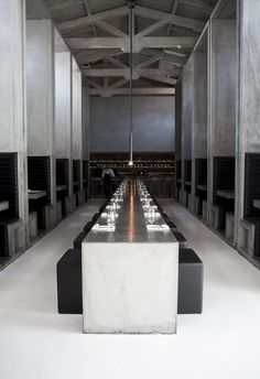 a long table with black chairs and white plates on it in the middle of an empty room