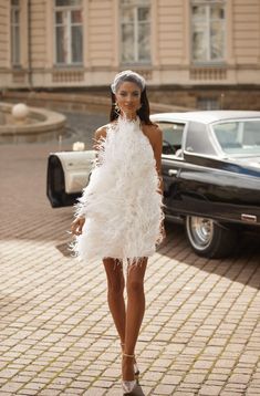 a woman is walking down the street wearing a white dress with feathers on her head