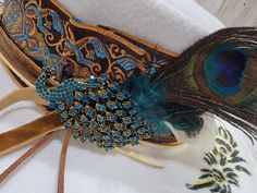 a close up of a peacock feather on top of a white cloth covered object with beads