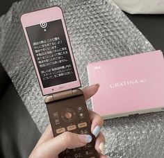 a person holding a cell phone in front of a pink box with writing on it