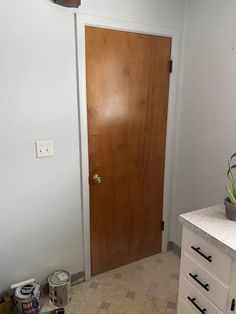 a bathroom with a wooden door next to a white cabinet and counter top under a light switch