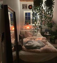 an unmade bed with plants hanging from the ceiling