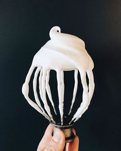 a hand holding a whisk with white icing on it