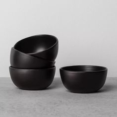 three black bowls stacked on top of each other in front of a white wall and floor