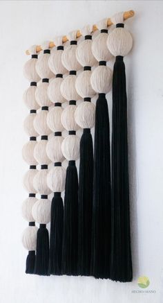 the wall hanging is decorated with black and white yarns, tassels and wooden pegs