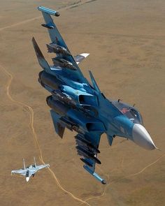 two fighter jets flying side by side in the air over dirt land and brown grass