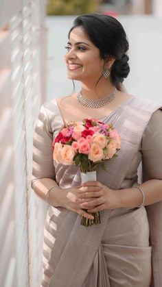 a woman in a gray sari holding a bouquet of pink and red flowers on her shoulder