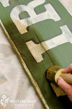 a person is painting the letters on a sign with a paintbrush and some wood