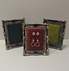 three framed pictures with two pairs of earrings in front of each other on a table