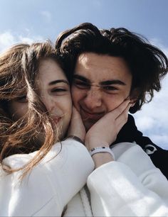 a man and woman embracing each other in front of the sky with clouds behind them