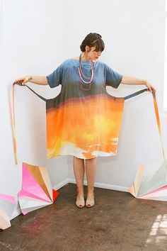 a woman standing in front of a wall holding onto two kites that look like they have been made out of paper