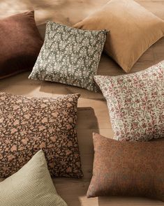 six pillows arranged in a circle on top of a wooden floor, all with different patterns and colors