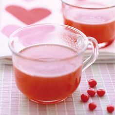 two glasses filled with liquid sitting on top of a table next to red candies