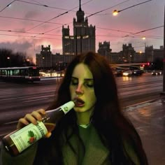 a woman with green makeup drinking from a bottle in front of a cityscape