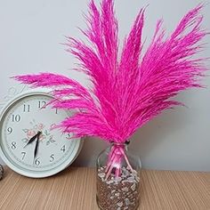 a pink flower in a vase next to a clock on a wooden table with other items