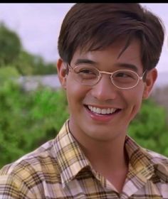 a young man wearing glasses and smiling at the camera with trees in the back ground