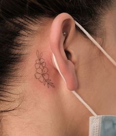 a woman's ear has a small flower tattoo on it