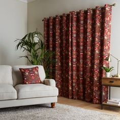 a living room with a couch, rug and window covered in red floral curtain panels