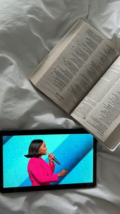 an open book sitting on top of a bed next to a cell phone and tablet