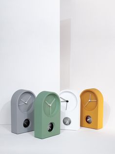 three different colored clocks sitting next to each other in front of a white wall and floor